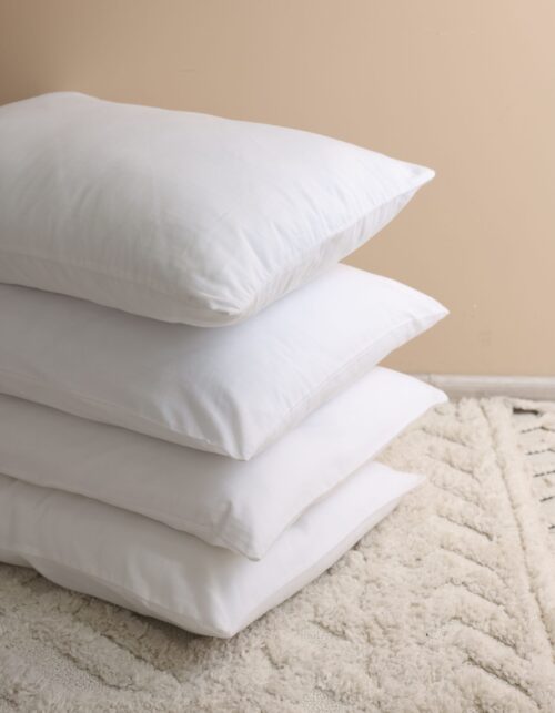 Stack of soft white pillows near beige wall indoors